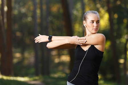 Portrait of young athletic woman wearing sporty clothes stretching and listening music in the sunny...