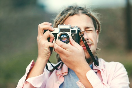 Hipster blonde bearded photograph boy with dreads taking pictures on the nature location in the forest, outdoor viewの写真素材