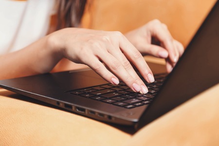 Cropped shot view of brunette girl laying on the yellow sofa in the light living room while working with her laptop, modern technology, communication conceptの写真素材