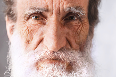 Portrait of contemporary cheerful bearded senior man with wrinkles in white shirt standing on the gray background, modern technology, communication conceptの写真素材