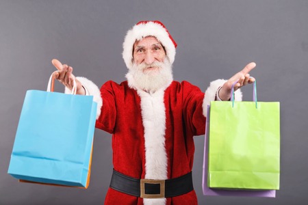 Santa Claus with a white beard wearing Santa outfit presents a lot of purchases on the gray background, New Year, Christmas, holidays, souvenirs, gifts, shopping, discounts, shopsの写真素材