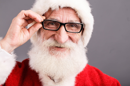 Portrait of Santa Claus with a white beard wearing glasses and Santa outfit standing on the gray background, New Year, Christmas, holidays, souvenirs, gifts, shopping, discounts, shopsの写真素材
