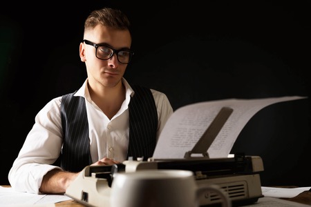 Book writer wearing white shirt sitting at the his workplace and using typewriter