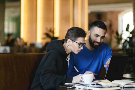 Male and female students watching training webinar and making notes with information for common...