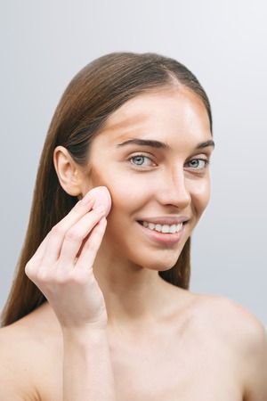 Woman applying foundation on her face using white beauty sponge