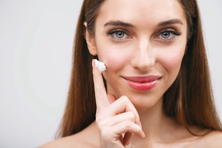 Young woman applying moisturizing lotion cosmetic cream on face for clean healthy soft skin careの写真素材