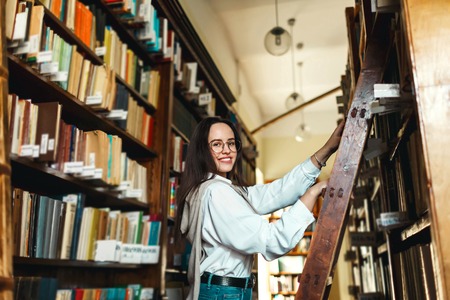 Student girl looking for books on shelves in the library
