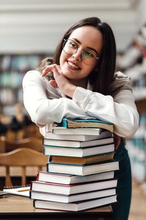 Portrait of brunette teen girl folding hands on the books in library