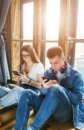 Two internet addicted students sitting with smartphones near the windowの写真素材