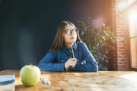 Brunette student girl wearing glasses holding pencil and looking to the windowの写真素材