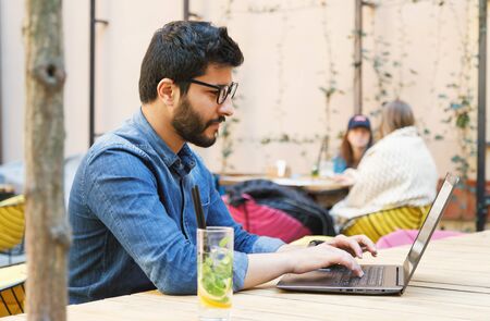 Multicultural smart student wearing glasses studying with laptop and drinking mohito at the cafeの写真素材