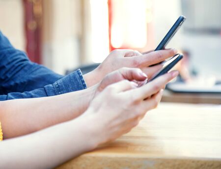 Close up view of two multicultural friends sitting at the cafe with their smartphones