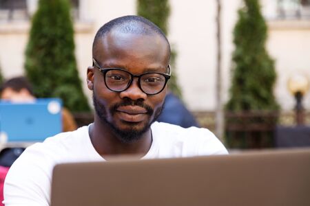 Portrait of african smart student wearing glasses using laptop while sitting at the cafe