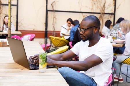 African smart student wearing glasses studying with laptop and drinking mohito at the cafeの写真素材