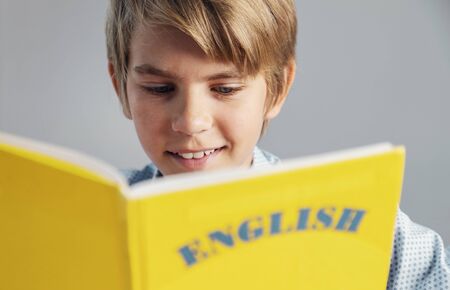 Close up view of blonde handsome preteen schoolboy holding yellow english book