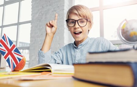 Young smart boy holding finger up in classroom, having an idea, learning english concept