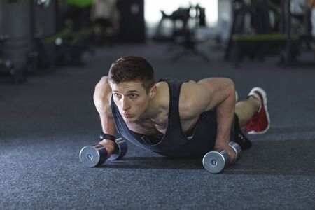 Athletic man in sportswear doing push-ups with the dumbbells at the gym
