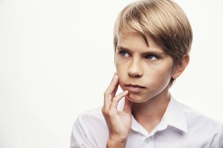 Blond boy thinking with his hand rubbing his cheek and chinの写真素材