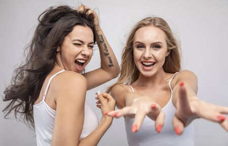 Playful young blonde and brunette having fun and stretching hands to camera isolated white backgroundの写真素材
