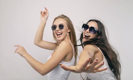 Cheerful young women in white tank tops and sunglasses dancing isolated white backgroundの写真素材