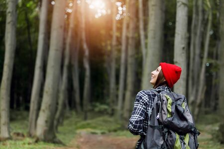 Back view of woman in casual outwear and with backpack walking on paved wood walkway in green woodsの写真素材