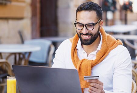 Portrait of masculine businessman in smiling and working on laptop while sitting in cafe outdoorsの写真素材