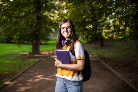 Portrait of joyful student girl on her way to classes via campus park pathの写真素材