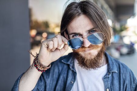 Portrait of young bearded man in mirrored sunglasses posing in a summer streetの写真素材