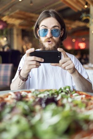 Young surprised male customer can not stop making and sharing the photo of the pizza servedの写真素材
