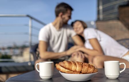 Morning coffee and croissants on a background of blurred young loving couple on balconyの写真素材