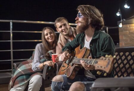 Young couple listening to their friends romantic guitar-accompanied song on a cozy balcony after sunsetの写真素材