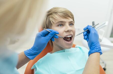 Blonde dentist examines the boys teeth with a mouth mirror and dental probeの写真素材