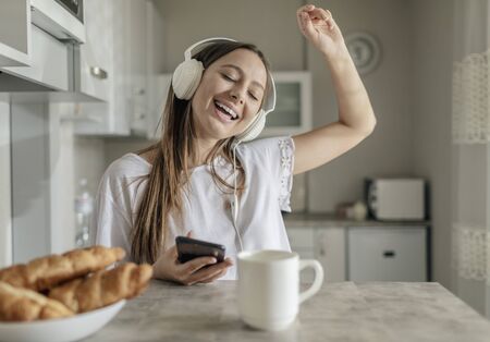 Young lady can not stop dancing while listening to the music alongside with breakfastの写真素材