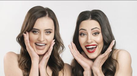 Portrait of smiling dark-haired girlfriends with naked shoulders showing surprise emotions isolated white backgroundの写真素材