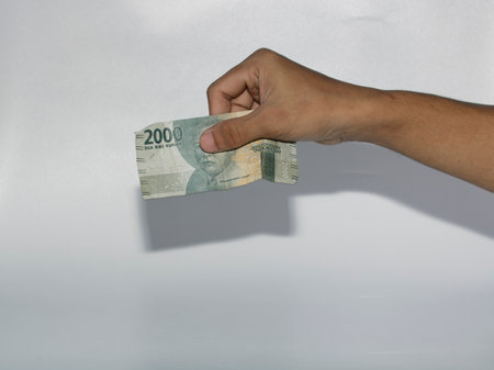Hand holding a twenty rupiah banknote on a white background with shadowのeditorial素材