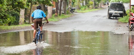 LAKE BATUR, BALI - JANUARY 21. Kid cycling through flooded street after downpour on Lake Batur on January 21, 2012 in Bali, Indonesia. Weather patterns have changed in recent years.のeditorial素材