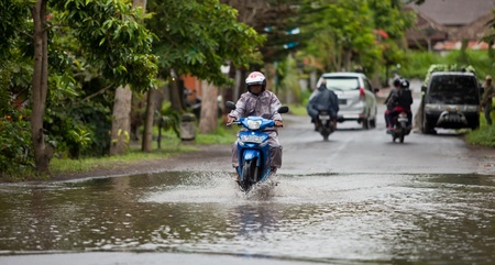 LAKE BATUR, BALI - JANUARY 21. Man driving through flooded street after downpour on Lake Batur on January 21, 2012 in Bali, Indonesia. Weather patterns have changed in recent years.のeditorial素材