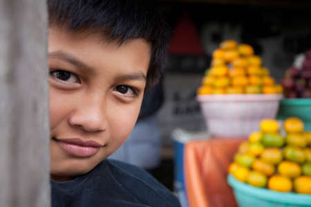 BALI - JANUARY 20. Son of a Balinese fruit stall owner family selling his postcards in Bali on January 20, 2012 in Bali, Indonesia. All family members participate in daily business.のeditorial素材