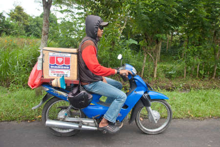 BALI - JANUARY 22. Balinese man carrying goods on bike in Bali on January 22, 2012 in Bali, Indonesia. Most Balinese people cannot afford cars and transport goods by motorcycle.のeditorial素材