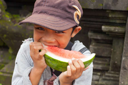 BALI - JANUARY 22. Young offering vendor eating watermelon at Mother Temple in Besakih on January 22, 2012 in Bali, Indonesia. It is common to share and eat the offerings at the end of the ceremony.のeditorial素材