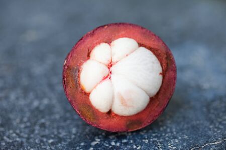 Open mangostin sitting on black volcanic rock bearing its white fleshの写真素材