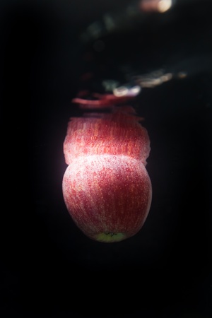 Red apple floating in water on black backgroundの写真素材