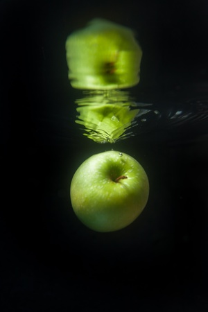 Green apple floating in water on black backgroundの写真素材