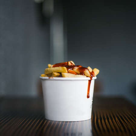 French fries in white cup filled with cheese on a wooden tableの写真素材