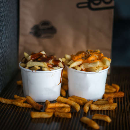 French fries in white cup filled with cheese on a wooden tableの写真素材