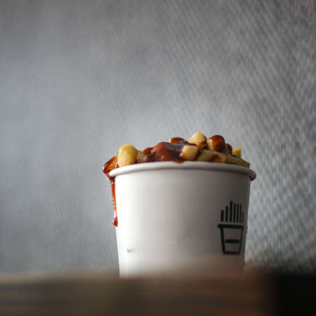 French fries in white cup filled with cheese on a wooden tableの写真素材