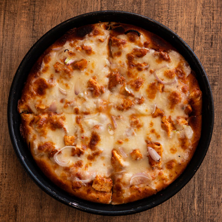 Chicken Tikka Pizza with Extra cheese on top and onion on a wooden tableの写真素材