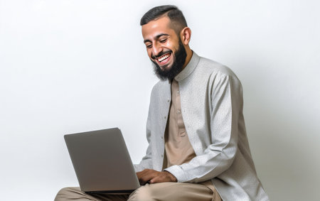 Portrait of a smiling arabian man using laptop while sitting against white backgroundの素材
