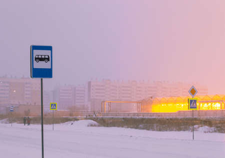 Bus stop sign against the background of the light of greenhouses, people and residential buildingsの写真素材