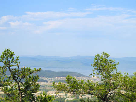 Pine branches against the background of the city below, lake and hills under a blue cloudy skyの写真素材